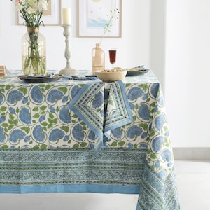 Könnte beinhalten: Ein Esstisch mit einer blau-grünen Tischdecke mit Blumenmuster und passenden Servietten. Der Tisch ist mit Tellern, einer Schüssel mit Nüssen und einer Vase mit Blumen gedeckt. Dekorative Kunstwerke hängen an der Wand.