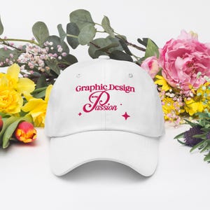 May include: White baseball cap with the text "Graphic Design is my Passion" in pink script. The cap is surrounded by colorful flowers, including yellow daffodils and pink peonies.