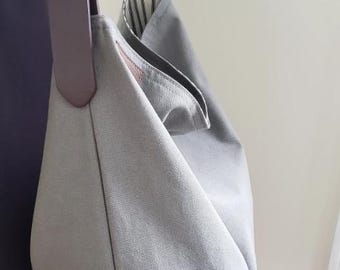 May include: A gray fabric shoulder bag with a brown leather strap and silver buckle. The bag has a unique, folded design and a striped interior lining. The strap is attached to the bag with a metal buckle.