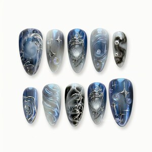 Puede incluir: Un conjunto de diez uñas artificiales con diversos diseños. Las uñas presentan una mezcla de colores azul, plateado y gris con patrones intrincados, incluyendo remolinos, formas geométricas y acentos metálicos. Las uñas son de forma ovalada.