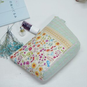 May include: A floral print cosmetic bag with a light green quilted exterior. The bag features a colorful pattern of flowers and birds. A bottle of nail polish and a small perfume bottle are next to the bag.
