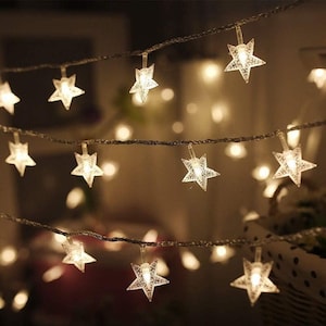 May include: String lights with clear, star-shaped bulbs. The lights are strung on a dark wire, creating a warm, inviting glow. The stars are evenly spaced and illuminated, perfect for festive decor.