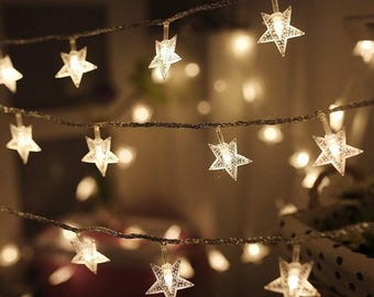 May include: String lights with clear, star-shaped bulbs. The lights are strung on a dark wire, creating a warm, inviting glow. The stars are evenly spaced and illuminated, perfect for festive decor.