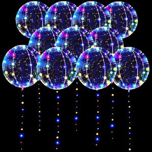Pode incluir: Um grupo de balões redondos e transparentes iluminados com luzes LED coloridas. Cada balão tem uma sequência de luzes penduradas, com pequenas luzes coloridas. Os balões estão em um fundo preto.