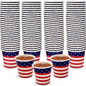 May include: Stacks of paper cups with a patriotic design. The cups feature a red and white striped pattern at the bottom, a blue band with white stars, and a white top. Some cups are filled with a brown liquid.