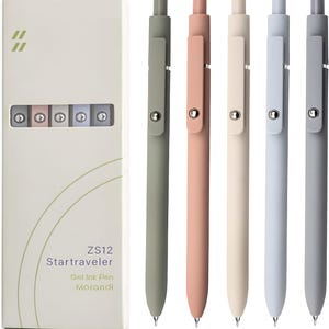 Puede incluir: Un juego de cinco bolígrafos de tinta gel en colores pastel, incluyendo verde, rosa, beige, azul y gris. Los bolígrafos se muestran junto a una caja blanca con el texto "ZS12 Startraveler Gel Ink Pen Morandi."