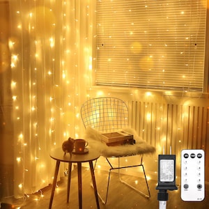 Peut inclure: Des guirlandes lumineuses blanc chaud illuminent une pièce, drapées sur un rideau transparent et une fenêtre. Une petite table d'appoint avec une tasse à café et un objet décoratif se trouve près d'une chaise en métal avec une fausse fourrure. Une télécommande est visible.