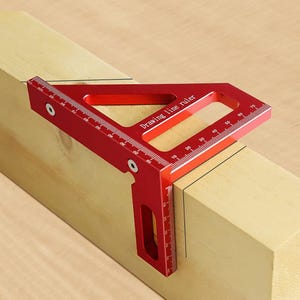 Puede incluir: Una escuadra de trazado roja de aluminio se coloca sobre un bloque de madera. La regla tiene medidas en centímetros y el texto "Drawing line ruler". La herramienta se utiliza para marcar líneas y ángulos.