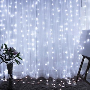 Peut inclure: Rideaux blancs illuminés par des lumières blanches, créant une ambiance chaleureuse. Les lumières sont uniformément espacées sur le tissu transparent. Un vase de fleurs est visible au premier plan. Les lumières sont sur un rideau blanc.
