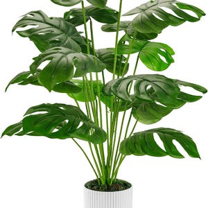 Puede incluir: Una gran planta artificial de monstera en una maceta blanca con nervaduras verticales. La planta tiene muchas hojas grandes, verdes con agujeros.