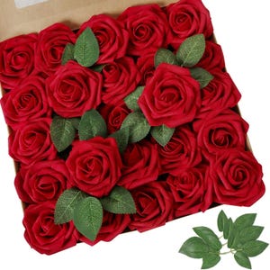 May include: A box filled with red silk rose flower heads. The roses are arranged in a circular pattern with green leaves interspersed throughout.