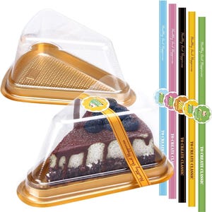 May include: A slice of cake in a clear plastic container with a gold base. The cake has a chocolate topping and blueberries. Colorful label stickers and ribbons with text are also visible.