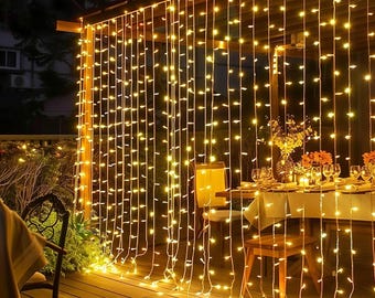 May include: Warm yellow string lights hanging from a wooden structure, creating a cozy ambiance. The lights are draped like curtains, illuminating a dining table set for a meal. The scene is set outdoors, with a dark background and a wooden deck.