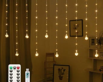 May include: Warm white LED string lights with star-shaped accents and spherical bulbs. Includes a remote control and USB connector. The lights are hanging in front of a curtain and a wall with framed art.