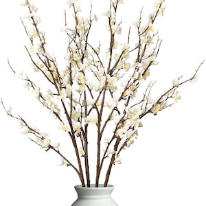 May include: A white ceramic vase displays a collection of artificial flowering branches. The branches feature dark brown stems and are decorated with small, delicate white blossoms. The vase has a simple, elegant design.