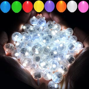 Puede incluir: Un puñado de pequeñas luces LED transparentes, cada una con un brillo blanco brillante, se sostiene en manos ahuecadas. Arriba, se muestra una fila de globos de colores en azul, verde, rojo, amarillo, morado, naranja, blanco y rosa. Estas luces son ideales para decoraciones de fiesta.