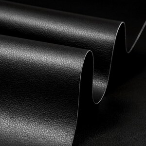 May include: Close-up of black faux leather fabric with a textured surface. The fabric is folded and curved, showing the texture and sheen.