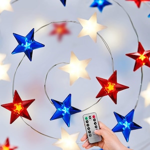 May include: A string of star-shaped lights in red, white, and blue. The lights are arranged in a spiral pattern, with a remote control in the foreground. The stars are made of a translucent material and emit a soft glow.