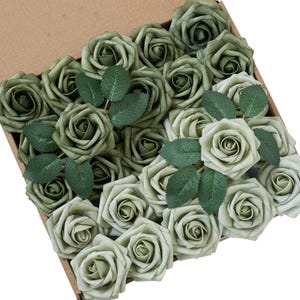 May include: A cardboard box overflowing with artificial roses in shades of green and sage. Each rose has detailed petals and is paired with green leaves. Suitable for crafting or decorative use.
