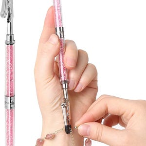 May include: A pink crystal-encrusted jewelry clasp tool with a silver clip. The tool is being used to fasten a pink beaded bracelet with a gold chain.