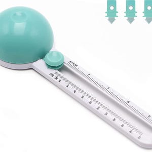May include: A white and teal circle cutter with a teal circle guide and a ruler marked in inches and centimeters. The ruler goes up to 32 inches or 80 centimeters.  The circle cutter has a small teal knob to adjust the size of the circle.