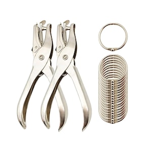 May include: Two silver metal hole punch tools for creating holes in paper for binding with metal rings. A stack of 20 silver metal rings for binding documents.