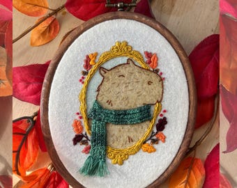 Herbst Capybara Stickrahmen – Fertiges handgemachtes Tierportrait Wandbild mit Schal und Herbstlaub in einem Goldrahmen
