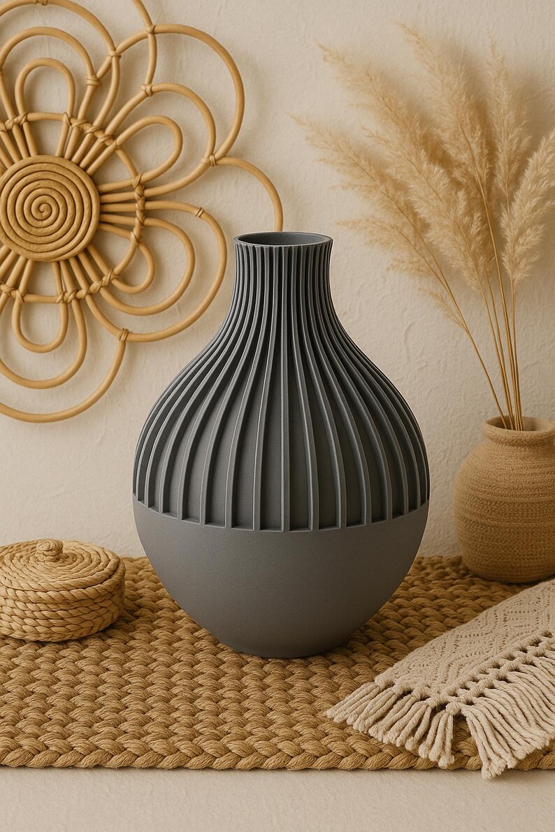 May include: A gray ceramic vase with a ribbed design sits on a woven mat. The vase is round and has a wide opening at the top. It is a modern and stylish vase that would look great in any home.
