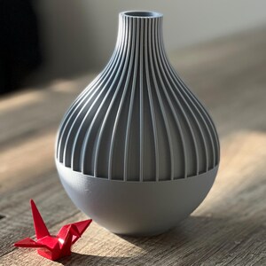 May include: A gray ceramic vase with a ribbed design. The vase is round and has a wide opening at the top. It is sitting on a wooden surface.