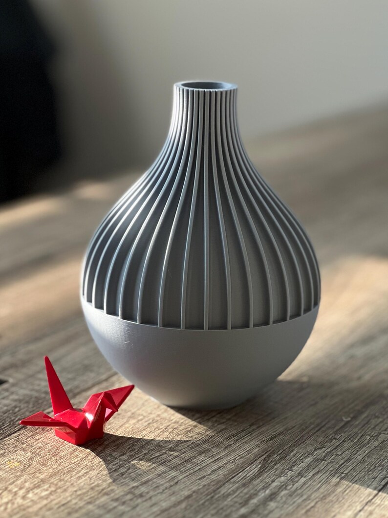 May include: A gray ceramic vase with a ribbed design. The vase is round and has a wide opening at the top. It is sitting on a wooden surface.
