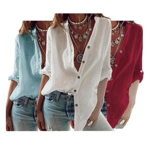 May include: Three button-down shirts in light blue, white, and red. The shirts have long sleeves that can be rolled up and are paired with blue jeans. Each shirt is unbuttoned at the top, revealing a layered necklace.