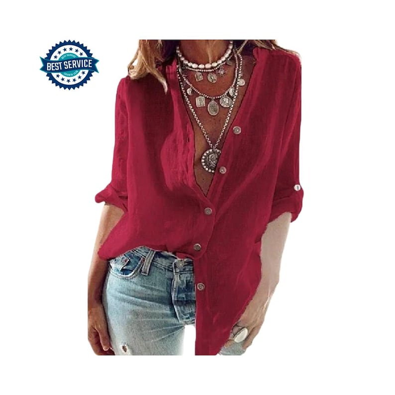 May include: A deep red button-down shirt with long sleeves, rolled up at the elbows. The shirt has a V-neck and is paired with light blue denim jeans. A multi-layered necklace is visible.