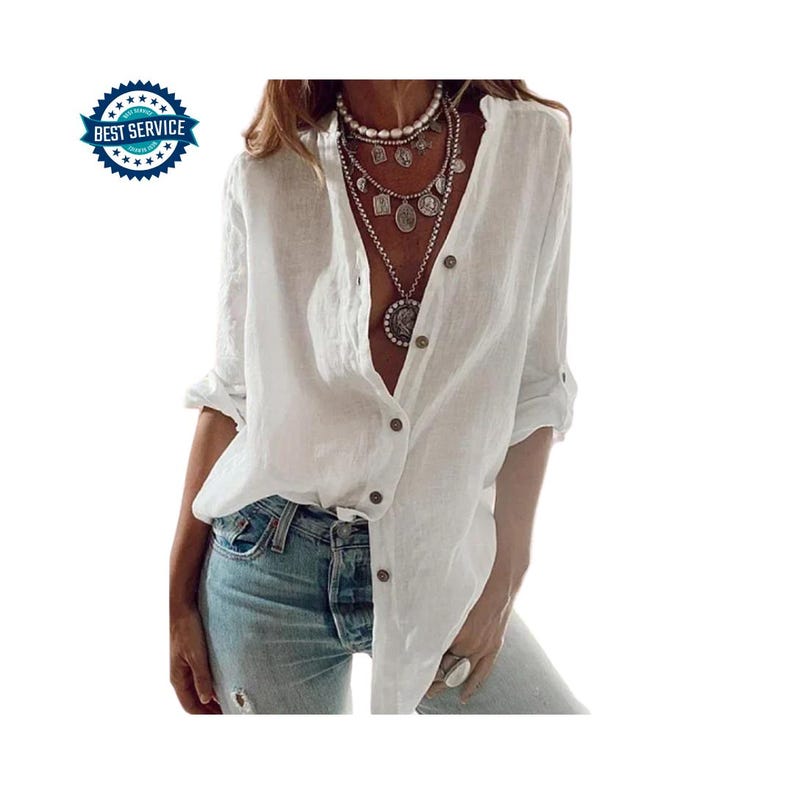 May include: A white linen button-down shirt with long sleeves, rolled up at the elbows. The shirt has a V-neck and is partially unbuttoned. The model is wearing blue jeans and multiple layered necklaces.