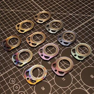 May include: A collection of 10 colorful metal keychains with a unique design. Each keychain has a different color and pattern, with a circular shape and a small hole for attaching keys.