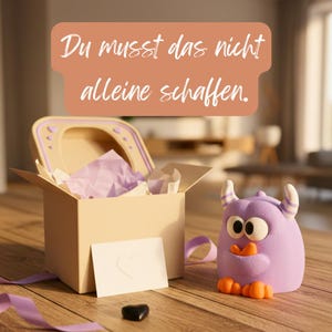 Könnte beinhalten: Eine skurrile Szene zeigt eine beige Box mit Deckel, gefüllt mit lila Seidenpapier. Ein kleines, lila Monster mit orangefarbenen Füßen und einem schnabelartigen Mund sitzt in der Nähe. Eine Karte mit einem Herzen und dem Text "Du musst das nicht alleine schaffen" ist ebenfalls vorhanden.