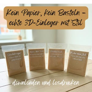 Könnte beinhalten: Vier kleine, beige Karten in transparenten Plastiktüten, jede mit weißem Text. Die Karten tragen Sätze wie "Happy New Year" und "Kleines Glück". Der obere Teil des Bildes enthält Text auf Deutsch. Die Karten liegen auf einer Holzoberfläche.