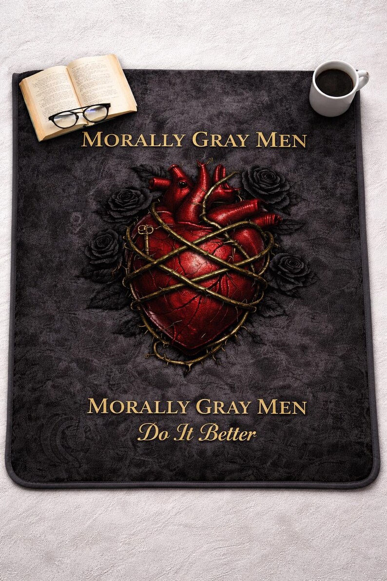 May include: A dark gray mat with a red anatomical heart design wrapped in barbed wire, surrounded by black roses. The text "MORALLY GRAY MEN" and "Do It Better" are in gold. A book, glasses, and coffee cup are also present.