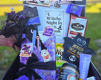 May include: A witch-themed gift box containing a selection of items. The box includes a candle, facial mask, tea, chocolate, socks, and other treats. The box is decorated with purple and black accents and the text "Limited Edition! Witchy Book Box Ships Free!"