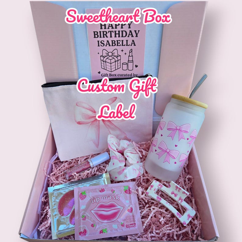 Puede incluir: Una caja de regalo rosa, etiquetada como "Sweetheart Box", llena de productos de belleza. Incluye un neceser, un vaso, una mascarilla labial, una goma para el pelo y una pinza para el pelo. La caja contiene una tarjeta que dice "Happy Birthday Isabella".