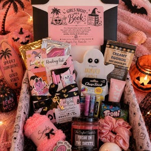 May include: A gift box containing a book wrapped in black ribbon with a gold key charm, a ghost-shaped face mask, a jar candle labeled Freak in the Sheets, pink fuzzy socks, a pink scrunchie, a bath bomb, hot chocolate mix, and lip balm.