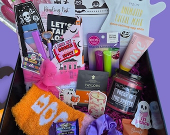 May include: A Halloween-themed gift box filled with self-care and relaxation items. Includes a ghost-shaped face mask, lip balm, a candle, a book, a towel with "BOO" on it, and other treats. The box is decorated with a pink bow and purple accents.