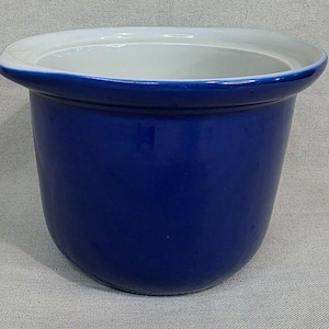 Może przedstawiać: Kobaltowa ceramiczna donica z białym wewnętrznym brzegiem. Donica ma zaokrąglony kształt z lekko rozszerzaną górą. Gładkie, błyszczące wykończenie odbija światło, podkreślając żywy niebieski kolor. Prosty, elegancki design.