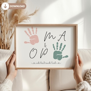Op de afbeelding: Een ingelijst print met een witte achtergrond en zwarte tekst. De tekst luidt "M A & O P" met een hartje en de tekst "ich hab euch lieb" eronder. Er zijn twee handafdrukken te zien, een roze en een groene.
