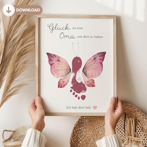 May include: A framed print with a butterfly design created from a footprint and handprint, in shades of pink and burgundy. The print displays the German text "Glück ist eine Oma wie dich zu haben" and "Ich hab dich lieb" with a heart symbol.