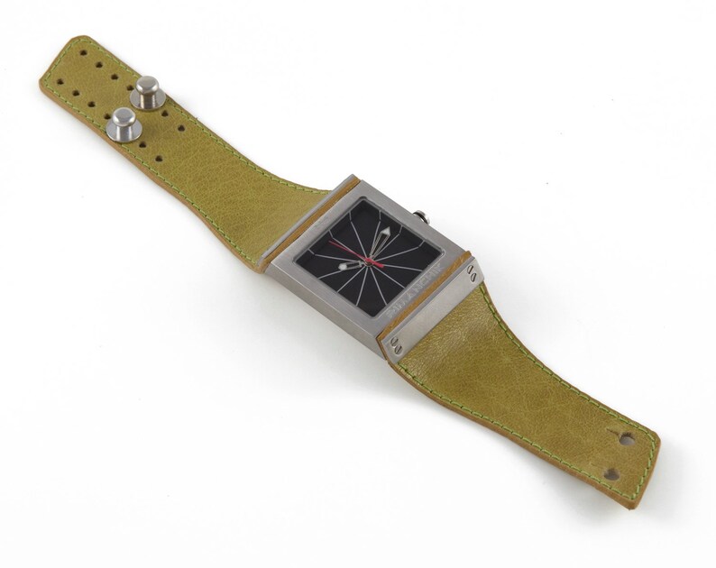May include: A square-shaped wristwatch with a black face and a green leather band. The watch has a unique design with a red hand and a black and white pattern on the face.