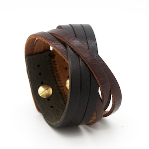 May include: A brown and black leather bracelet with a braided design and a brass buckle.