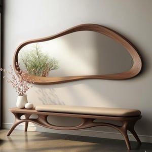 May include: A modern, organic-shaped wooden mirror with a shelf is mounted on a neutral wall. Below, a matching wooden bench with a beige cushion complements the mirror. The room is decorated with a vase of flowers.