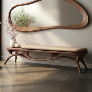 Pode incluir: Um banco de madeira moderno com uma almofada bege, apresentando um design curvo único. Acima, um grande espelho de madeira com formato orgânico está pendurado na parede. A cena é complementada por um vaso de flores e um pequeno objeto decorativo no banco.