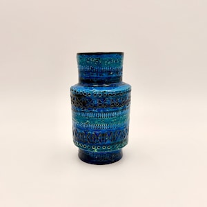 May include: A vintage ceramic vase with a textured surface and a vibrant blue color palette. The vase features a cylindrical shape with decorative bands of geometric patterns in shades of blue and black. The vase is approximately 10 inches tall.