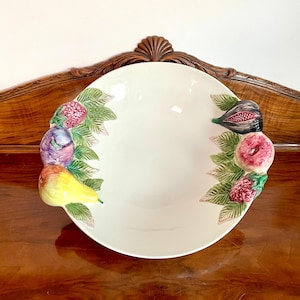 Könnte beinhalten: Eine weiße Keramik-Servierschüssel mit farbenfrohen Fruchtakzenten. Die Schüssel zeigt eine Birne, Feigen und Himbeeren mit grünen Blättern. Die Schüssel steht auf einer Holzoberfläche.